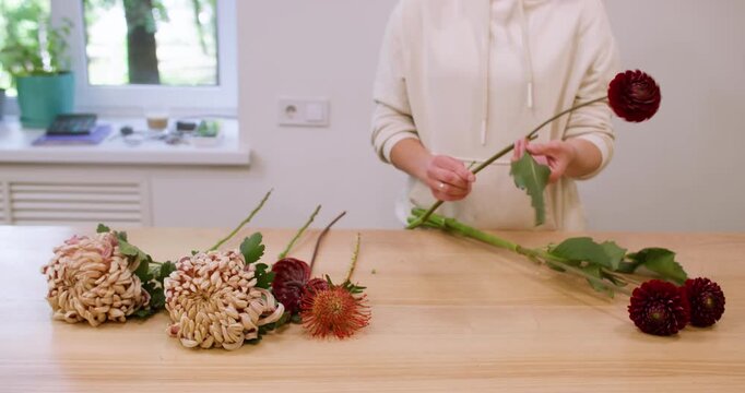 Florist working. Autumn flower. Unrecognizable professional female arranging seasonal chrysanthemum bouquet at wooden table in shop.