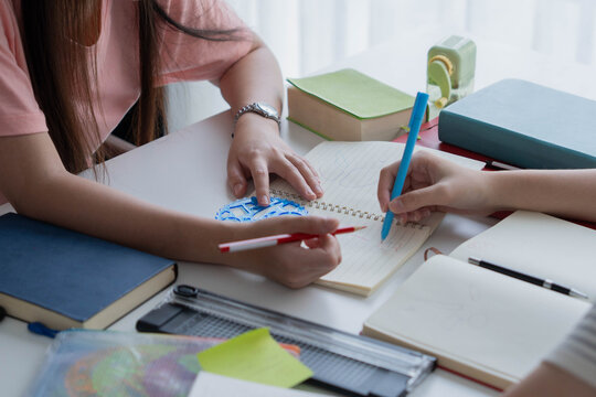 Two Asian girl with books on table doing homework together at home