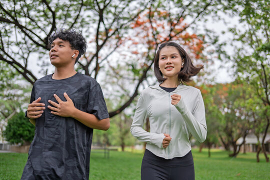 Multicultural Gen Z friends Asian Gen Z woman and African American mixed race man running together in urban park for wellness and active lifestyle.