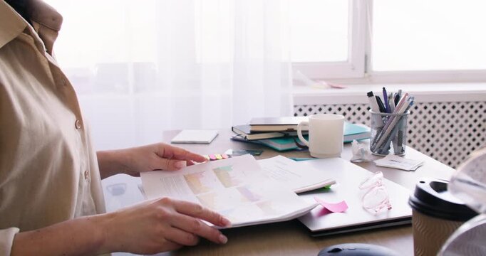 Freelance paperwork. Remote occupation. Unrecognizable woman entrepreneur preparing for job at desk with laptop writing notes indoor.