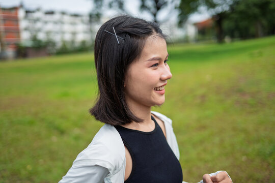 Asian Gen Z woman jogging in green urban park for wellness fitness and active city lifestyle