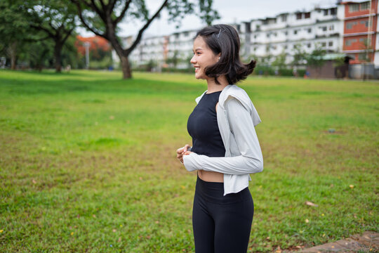 Asian Gen Z woman jogging in green urban park for wellness fitness and active city lifestyle