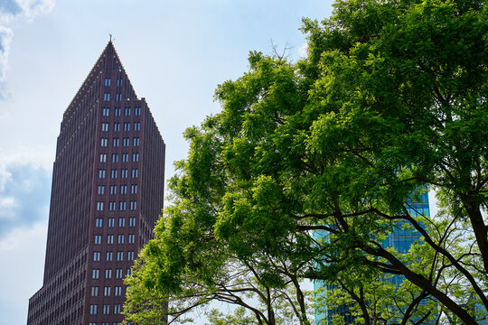 Low angle view of a modern office tower with green trees on a sunny day. Concept of contemporary architecture, commercial real estate and sustainable urban development