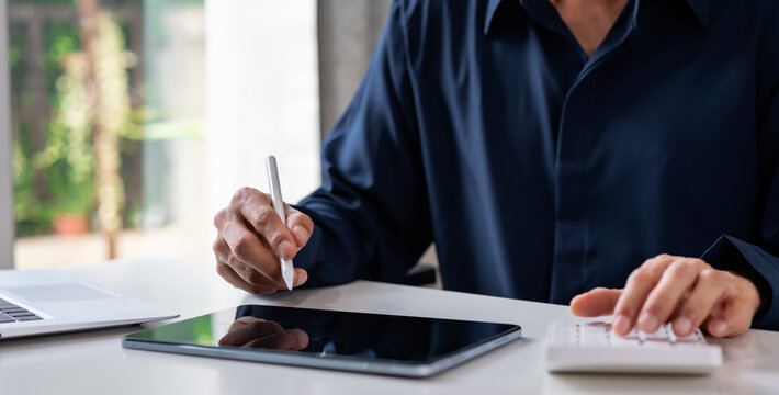 Close-up of a businessman using a stylus pen on tablet with calculator at a desk, Digital data entry and accounting concept