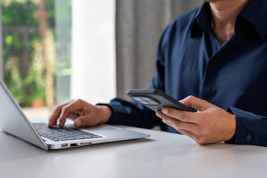 Young male working with smartphone and laptop at a modern home office desk