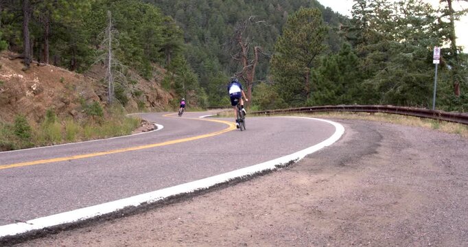 Pair of cyclists quickly pass by on winding mountain road.