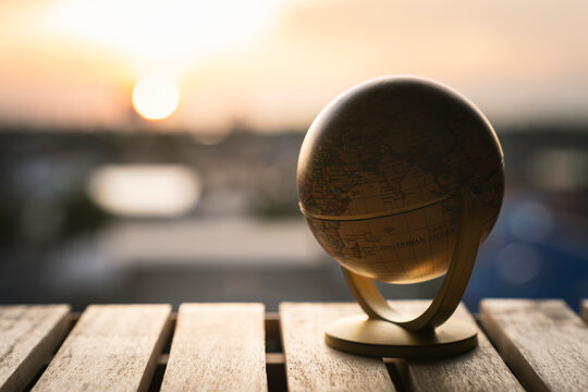Global business concept with small globe model on wooden table at sunset for international trade, travel destination, worldwide network and earth environment.