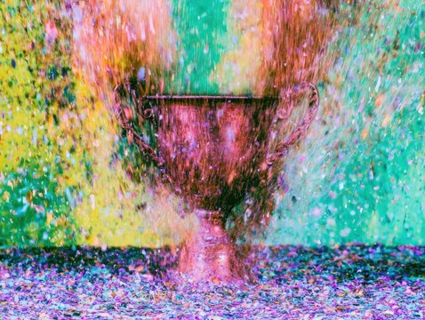 Ornate rose gold ceremonial trophy cup centered amidst exploding rainbow confetti for victory celebration and achievement concepts