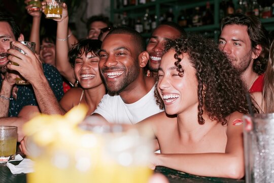 Animated group of young adults laughing at a crowded bar with cocktails, featuring candid joy and a moody flash aesthetic for nightlife social content