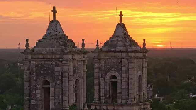 Aerial drone view of the San Gervasio Cathedral and its twin bell towers in Valladolid, Yucatan, Mexico, glowing under a warm golden-hour sky.