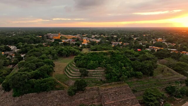 Aerial view of the green colonial town of Izamal, Yucatan, Mexico, in soft twilight, warm light lingering over rooftops and tropical trees.