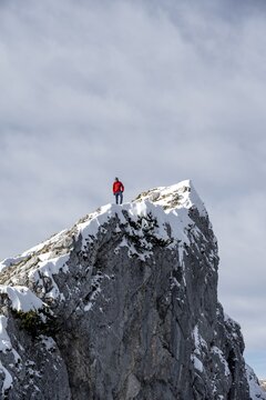 Mountaineer with red jacket on a rock spire, mountains in winter with snow, hiking to Ammergauer Hochplatte in the Ammergau Alps, Bavaria, Germany