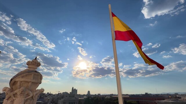 Beautiful spanish flag waving proudly in the wind against a blue sky with clouds over the city of Madrid, embodying a strong sense of national pride and patriotism on a sunny day