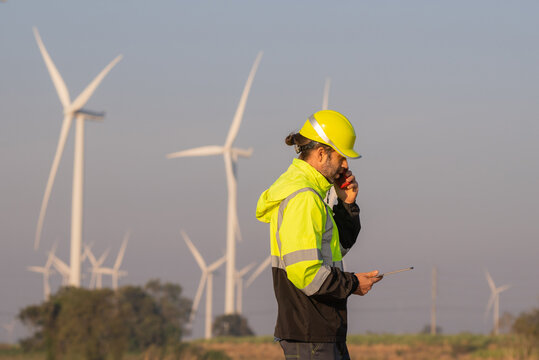 Engineers male flying drone surveying and checking wind turbines from the high angle view of the field during beautiful sunset. using drone technology for work.