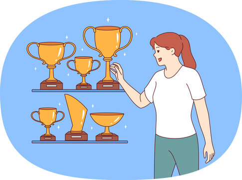Woman leader stands near gold awards and cups won in sports competitions or professional competitions. Girl leader is proud to have trophies earned for outstanding results in business