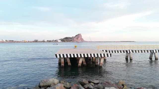 View of the entrance to Mazatlan Harbor from the pier, featuring a small fishing boat crossing calm waters toward Stone Island (Isla de la Piedra), with Cerro de los Chivos in the background.