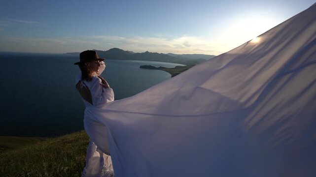Woman dress mountain, stylish young woman in white flowing dress posing on scenic cliffside at sunset with beautiful ocean and mountains in background