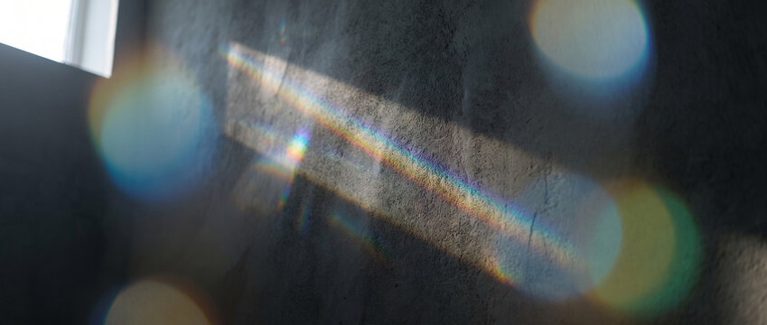 Rainbow prism light leak on concrete wall with vibrant spectrum colors, soft circular bokeh, and moody shadow textures, perfect as an atmospheric background for creative design projects