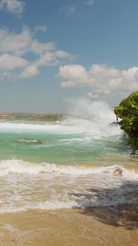 Vertical video. Tropical Beach Cove With Waves Rolling Between Rocky Cliffs and Lush Green Vegetation in Slow Motion