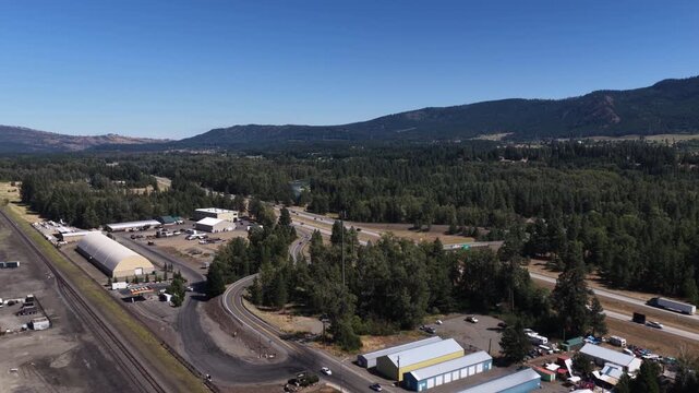 Aerial of commercial corridor train tracks and highway interchange in Cle Elum Washington with dense forest backdrop in Wenatchee National Forest
