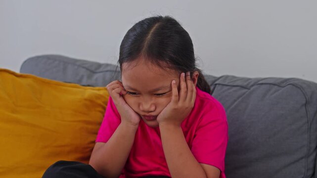 Sulking little girl looking down with angry, bored expression on sofa