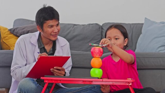 Child psychologist in white coat guiding young girl patient through educational game on small table