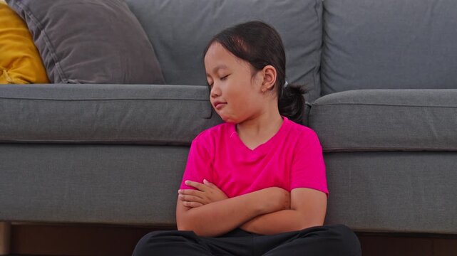 Disappointed young girl sitting by sofa with folded arms showing resentment