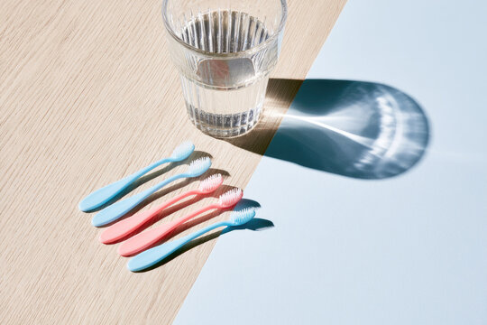 Interdental brush teeth set pastel color clear glass water light oak surface morning daylight minimalist dental care aesthetic clean shadow copy space