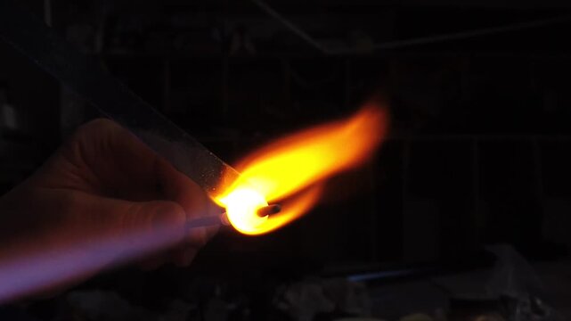 Slow motion view of artist hands shaping glass bead holding it over a gas torch in a workshop. Glass work jewelry