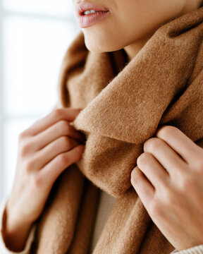 Scarf neck hands adjusting wool collar close up warm indoor portrait soft lighting natural skin texture cozy winter comfort calm expression