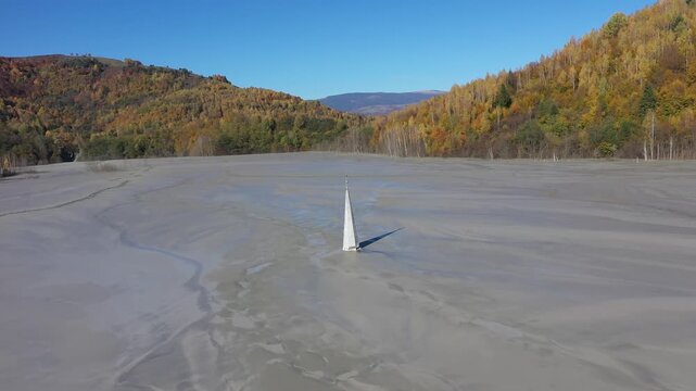Aerial slow motion view of a church tower with cross, buried under mud in decanting lake
