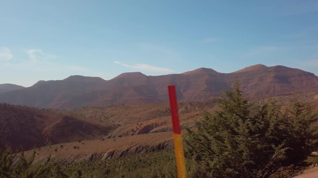 Tizi n'Tichka in Morocco's High Atlas Mountains with a winding mountain pass through rugged red peaks, barren valleys and semi-arid terrain under a clear blue daytime sky.
