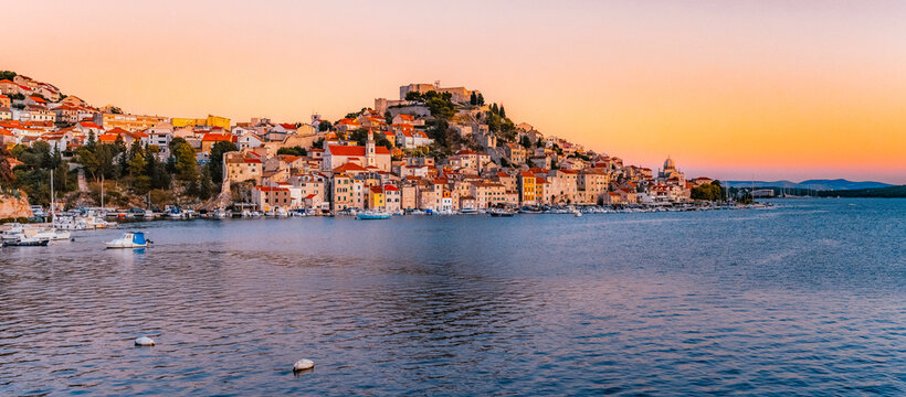 evening at Banj beach with a view of the historic Sibenik city center and fortress under a colorful sunset sky, Croatia.