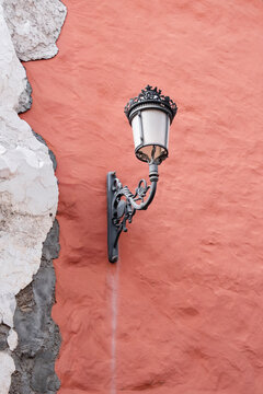 An ornate vintage black lantern is mounted on a textured terracotta wall with peeling white plaster. 