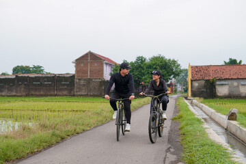 Obraz premium Asian Couple Cycling Through Rural Landscape in Indonesia