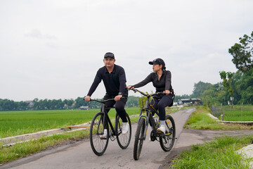 Fototapeta premium Asian Couple Cycling Through Rural Landscape in Indonesia