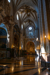 Obraz premium Wide vertical view along the side aisle of the Cathedral of San Salvador, La Seo in Zaragoza, Spain, featuring polished marble floors, gothic ribbed vaults, side chapels, and a distant gilded altarpie