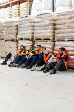 Group of tired multi ethnic warehouse workers resting on the floor during a demanding shift at a logistics distribution center