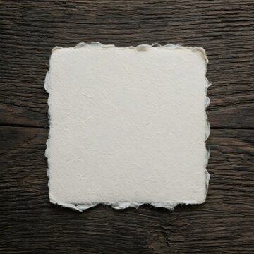 Blank square sheet of handmade deckle edge paper on a rustic dark wooden background