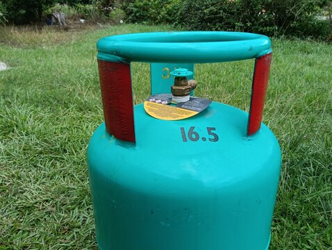 A green 16.5 kg LPG gas cylinder placed upright on a grassy field outdoors. The steel liquefied petroleum gas cylinder features a protective ring around the valve . in malaysia