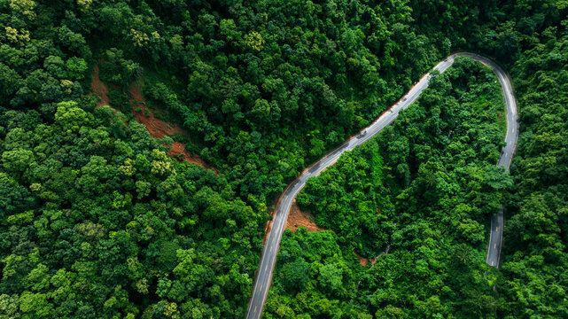 Aerial drone view of a winding mountain road partially blocked by a landslide after heavy rainfall. Dense tropical rainforest surrounds damaged infrastructure, illustrating natural disasters, climate