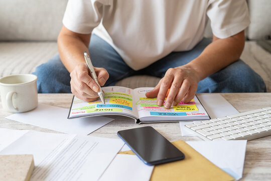 Person organizing commitments and tasks in a detailed planner with sticky notes, managing personal finance, budgeting, and controlling expenses for an efficient daily life