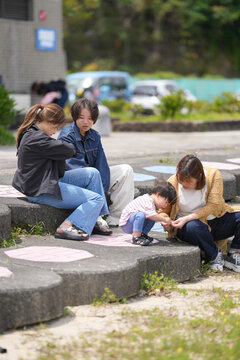 Family enjoys quiet time outdoors on stone steps. Child giggles as adults sit nearby, sharing warmth. Sunlit setting evokes calm and connection. Ideal for family, parenting, or community moments