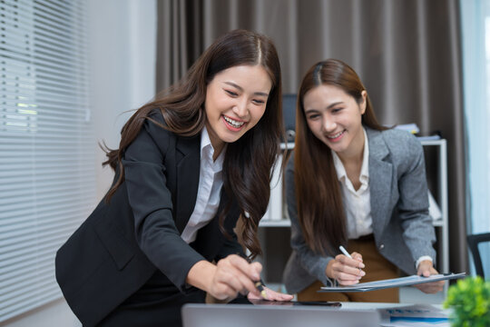  Two professional women work together at a desk, reviewing information on a laptop, collaborating on teamwork and business planning, and analyzing data.