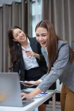 Two professional women work together at a desk, reviewing information on a laptop, collaborating on teamwork and business planning, and analyzing data.