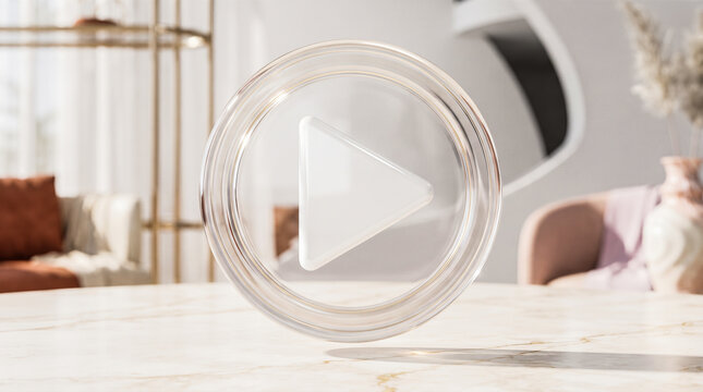 Transparent glass play button icon standing on marble table inside luxury contemporary domestic space with blurred furniture and soft sunlight entering through windows