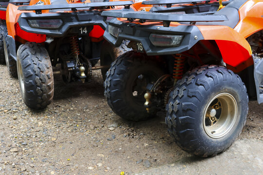 Orange all terrain vehicles parked on muddy gravel with visible suspension and rugged tires, outdoor rental fleet ready for adventure and durable off road use
