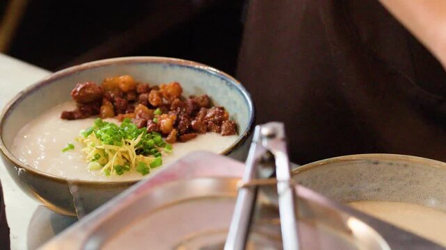 Asian Chef Garnishing Rice Congee with Scallions and Ginger