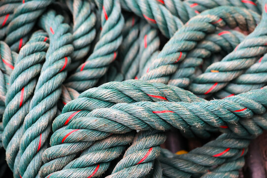 Thick twisted green rope with red tracers coiled in textured tangle showing fiber detail and weathered surface, conveying nautical utility and rugged tactile character