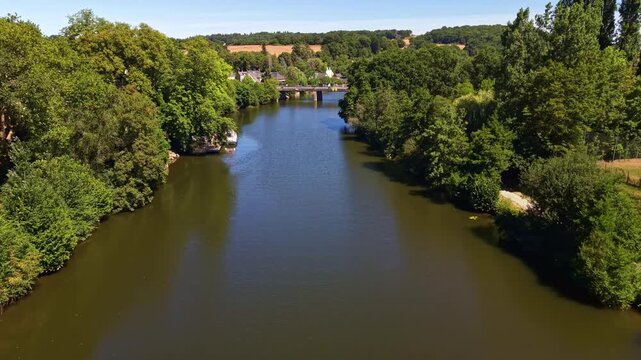 Drone flies above the tree-lined Mayenne River on a sunny day in Chang&eacute;, France.
